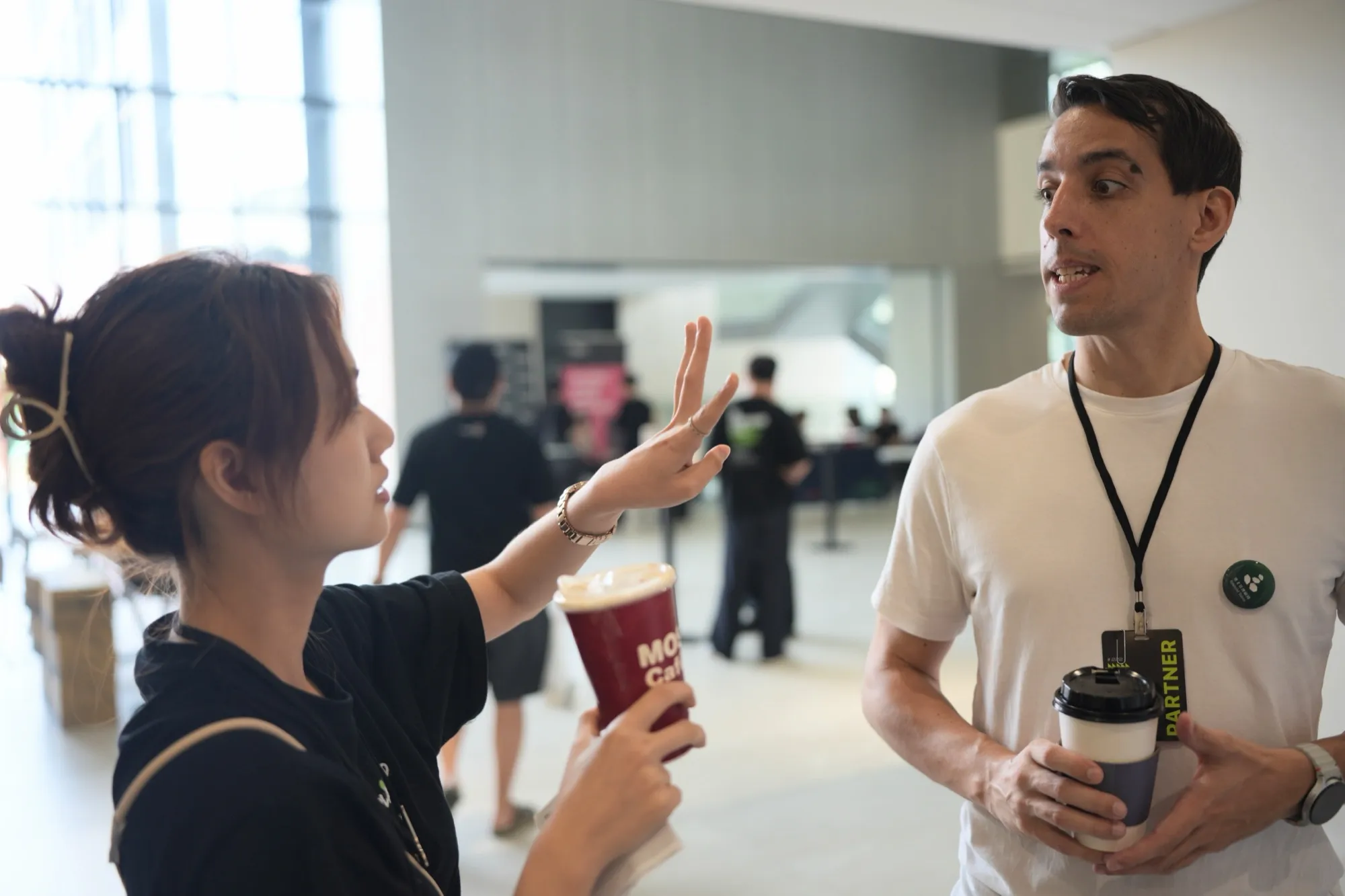 iPlayground 2026 Day 2 黑衣參與者拿著飲料，與一位夥伴在會場自然交談